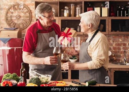 Romantic senior couple exchanging gifts and drinking wine in kitchen Stock Photo