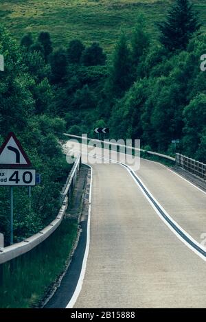 Winding rural road leading through green hills and forest in Scotland, UK. Stock Photo