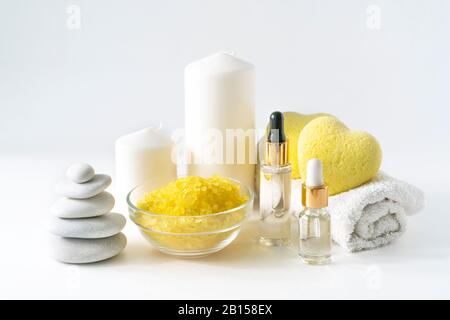 Relaxing bath products composition with yellow heart shaped bath bombs, sea salt scrab, body serum, candles, towel and stone stack on a light background. Relaxation, spa and body treatment concept. Stock Photo