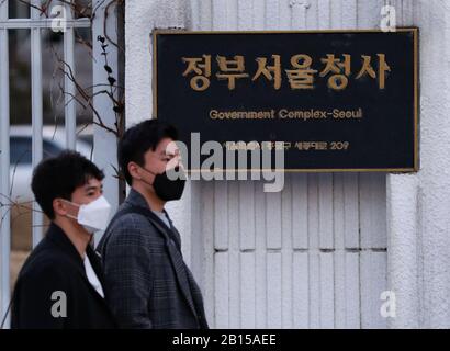 Seoul, South Korea. 23rd Feb, 2020. Pedestrians walk past the government complex in Seoul, South Korea, Feb. 23, 2020. South Korea raised its four-tier virus alert to the highest 'red' level on Sunday as the number of COVID-19 infection cases soared to 602 in recent days with the death toll rising to five. Credit: Xinhua/Alamy Live News Stock Photo