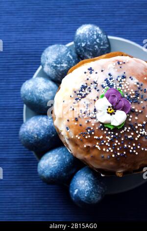 Easter cake decorated with sugar flower and blue colored eggs on a plate on blue cloth background. Eggs were colored blue with a hibiscus decoction. F Stock Photo