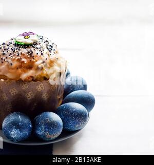 Easter cake decorated with sugar flower and blue colored eggs on a plate on white and blue clothbackground with copy space. Eggs were colored blue wit Stock Photo
