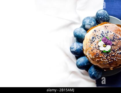 Easter cake decorated with sugar flower and blue colored eggs on a plate on white and blue cloth background with copy space. Eggs were colored blue wi Stock Photo