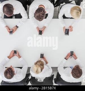Business people using smartphones sitting at table in office, white copy space background Stock Photo