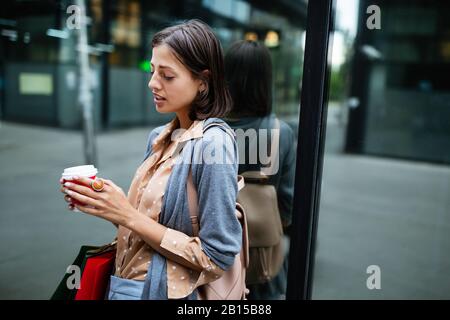 Happy young woman drinking take away coffee and walking with bags after shopping in city. Stock Photo