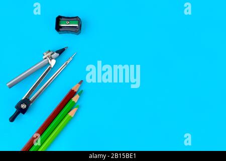 A black pencil sharpener along side a pencil attached to a pencil compass and some different colored pencil crayons on a blue paper background Stock Photo