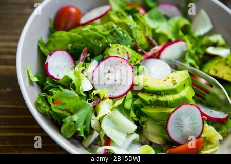 Healthy salad closeup. Clean eating , vegan vegetarian healthy salad with radish, beetroot, lettuce, cherry tomatoes, avocado, green onion and spices Stock Photo