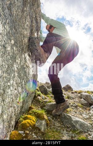 Female mountaineer practicing boulder climbing outdoor on large boulder. Stock Photo