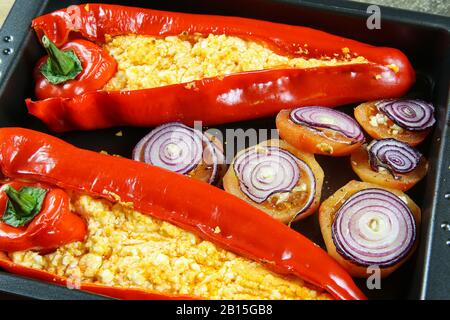 Close up of two baked red bell peppers filled with spicy chili feta and tomatoes with onion rings on oven tray Stock Photo