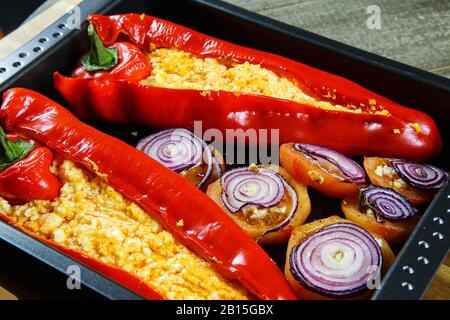 Close up of two baked red bell peppers filled with spicy chili feta and tomatoes with onion rings on oven tray Stock Photo