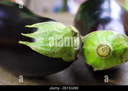 Macro close up of two isolated aubergines on wood table (focus on plant stem left) Stock Photo