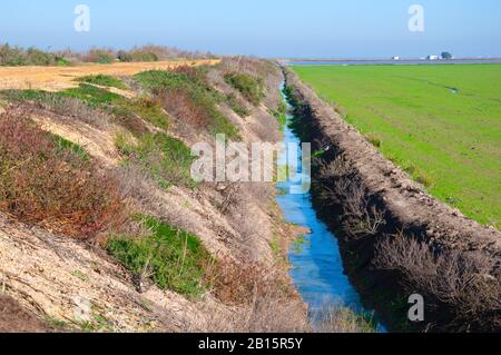 Small canal with water between road with dry grass and green field. Spring in Seville, Spain Stock Photo