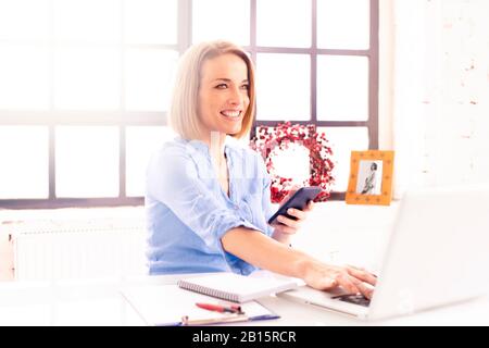 Shot of happy mature businesswoman text messaging while working on laptop in the office. Stock Photo