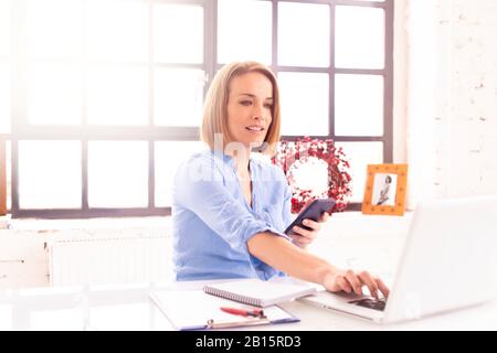 Shot of happy mature businesswoman text messaging while working on laptop in the office. Stock Photo