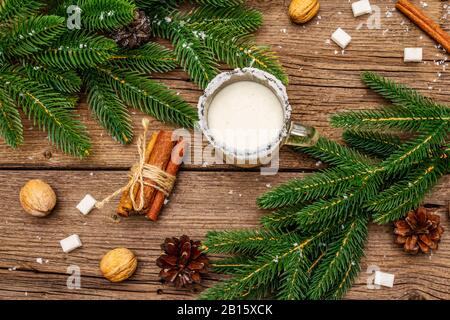 Christmas eggnog liqueur or cola de mono cocktail. Classical winter drink in glass mug, xmas decorations. Evergreen branches, cinnamon, walnuts, sugar Stock Photo
