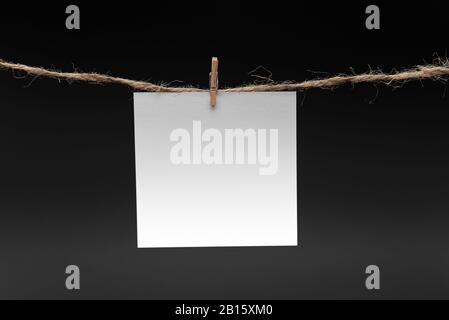 Blank Paper, hanging on rope by pin against black background, concept, office Stock Photo