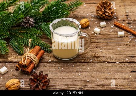 Christmas eggnog liqueur or cola de mono cocktail. Classical winter drink in glass mug, xmas decorations. Evergreen branches, cinnamon, walnuts, sugar Stock Photo