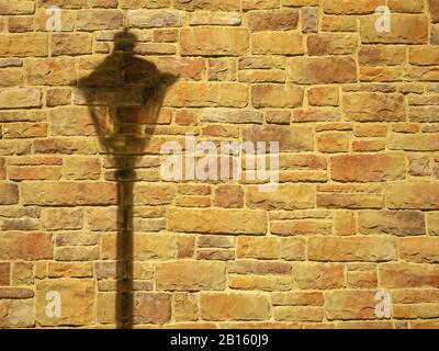Photo of an illuminated orange-yellow brick wall with falling shadow from a lantern on it Stock Photo