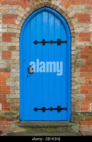 Traditional blue arched door with black ironmongery in a doorway, UK Stock Photo