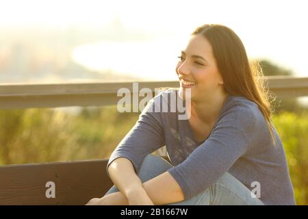 Happy woman smiling and relaxing sitted on a bench with views on the background