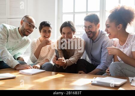 Five laughing multi-ethnic friends having fun using smartphone Stock Photo