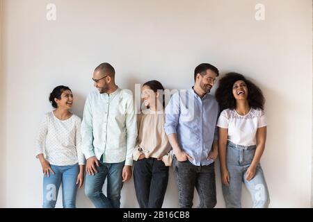 Five diverse best friends standing near wall indoors and laughing Stock Photo
