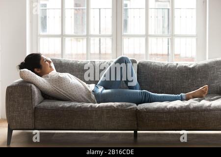 Woman lying on couch putting hands behind head enjoy vacation Stock Photo
