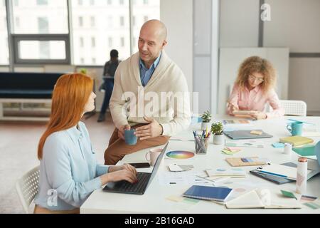 Portrait of balding mature businessman talking to women during coffee break in modern office, copy space Stock Photo