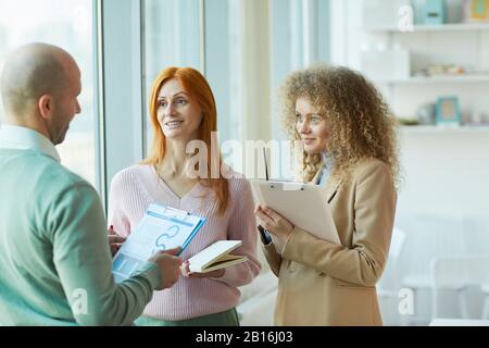 Waist up portrait of three business people discussing work project while standing by window in office, copy space Stock Photo