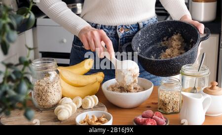 Woman putting oatmeal in a bowl with spoon. Preparing healthy breakfast at the kitchen. Healthy lifestyle concept Stock Photo