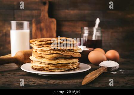 Blini, russian thin pancakes or crepes stacked on plate over rustic composition. Concept of traditional holiday Maslenitsa or Shrove Tuesday Stock Photo