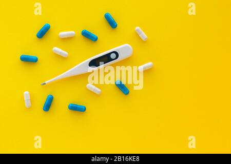 Digital thermometer and pills/capsules isolated on bright yellow background. Medicine, epidemic, painkillers, healthcare and treatment concept. Flat l Stock Photo