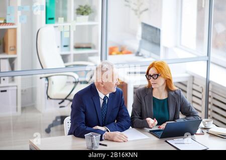 High angle view at two senior managers discussing work issues while sitting together at desk in empty office, copy space Stock Photo