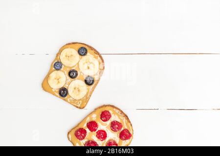 Peanut butter toast with banana, blueberry and raspberry on white wooden table with copy space Stock Photo