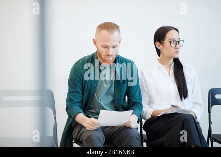 Portrait of two young people waiting in line for job interview and reviewing notes , copy space Stock Photo