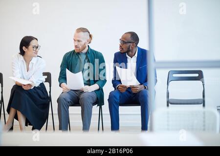 Multi-ethnic group of young people waiting in line for job interview and chatting behind glass wall , copy space Stock Photo