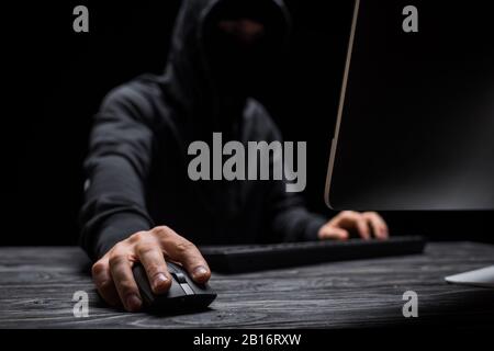 selective focus of computer mouse in hand on hacker isolated on black Stock Photo