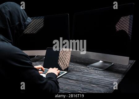 hacker using laptop with blank screen near computer monitors isolated on black Stock Photo