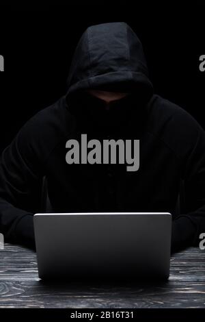 anonymous hacker in hood using laptop isolated on black Stock Photo