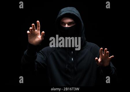 anonymous hacker in hood gesturing isolated on black Stock Photo