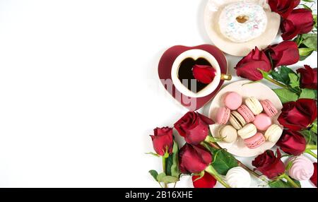 Red roses and morning tea creative composition flat lay layout with coffee in heart shaped cup and saucer and macarons and donuts on white background, Stock Photo
