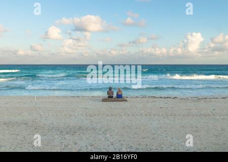 Two women sitting on a tree at the ocean with turquoise water during sunset at Cancun, Yucatan, Mexico Stock Photo