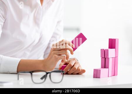 Selective focus of businesswoman stacking marketing pyramid from pink blocks wood game on table Stock Photo