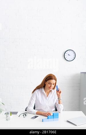 Businesswoman making marketing pyramid from blue building blocks near gadgets on table Stock Photo