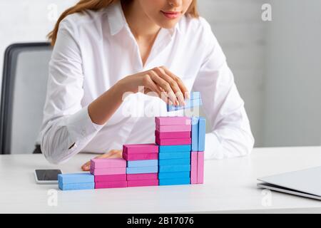 Cropped view of businesswoman stacking marketing pyramid from building blocks on table in office Stock Photo