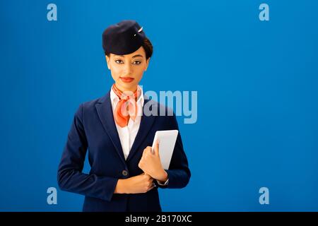 smiling african american flight attendant holding digital tablet isolated on blue Stock Photo