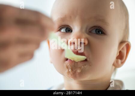 Selective focus of mother feeding baby with puree on grey background Stock Photo