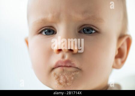 Portrait of sad baby boy with puree on soiled mouth isolated on grey Stock Photo