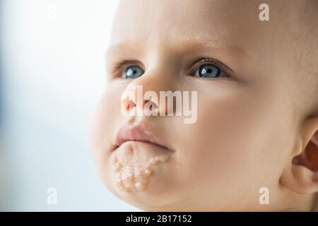 Portrait of cute infant with soiled mouth with baby food isolated on grey Stock Photo