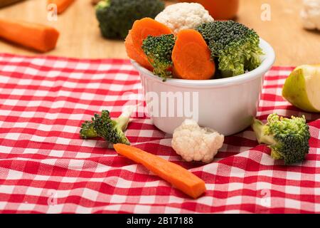 Close up view of fresh vegetables in bowl on checkered tablecloth on wooden background Stock Photo